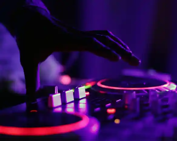 A close-up of a hand adjusting a DJ mixer with glowing knobs and buttons in purple lighting.