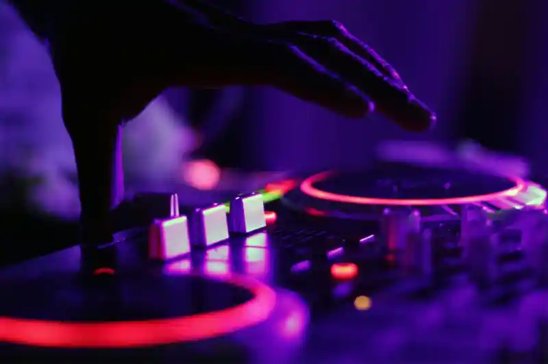 A close-up of a hand adjusting a DJ mixer with glowing knobs and buttons in purple lighting.