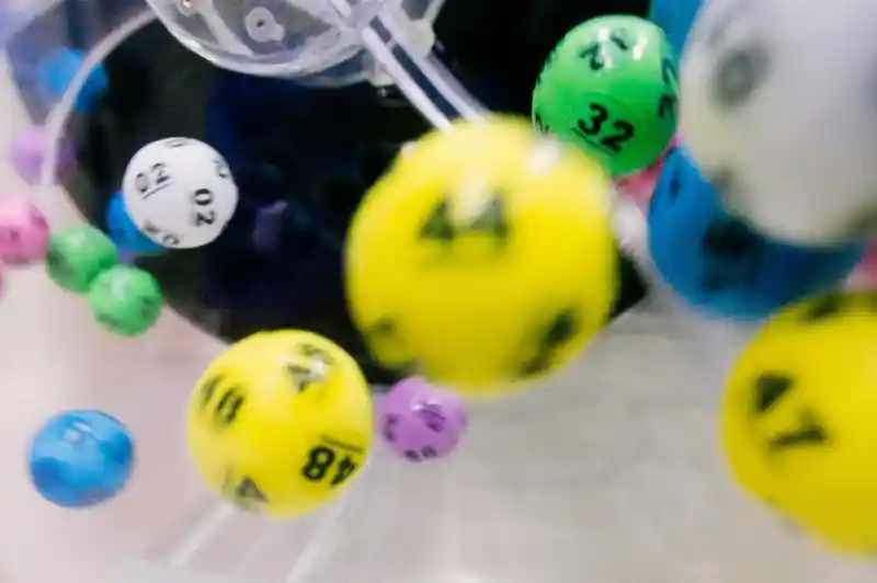 Colorful lottery balls in motion, with numbers ranging from 02 to 49, captured inside a lottery drawing machine.