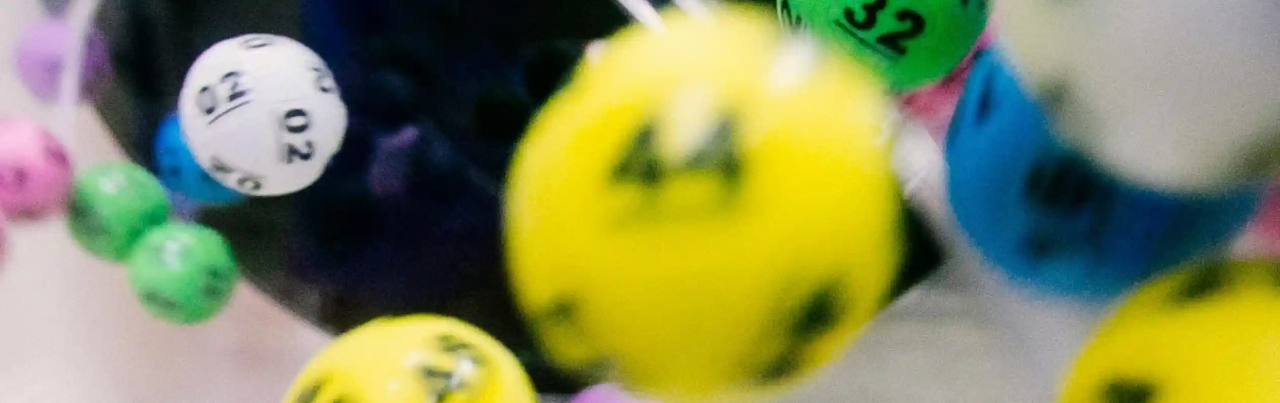Colorful lottery balls in motion, with numbers ranging from 02 to 49, captured inside a lottery drawing machine.
