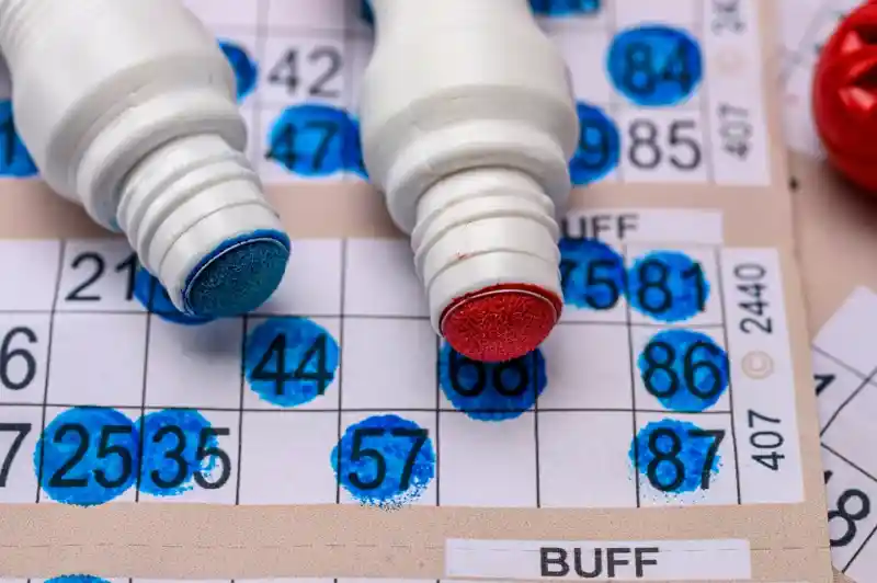 A Bingo card sheet with red and blue bingo dabber pens.