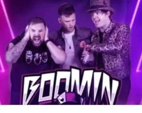 Three men are posing dramatically against a vibrant purple background with neon lighting. One man covers his ears with a distressed expression, the second stands in the middle looking surprised, and the third is wearing a leopard-print jacket and a hat, playfully holding a toy gun. The word "BOOMIN" is prominently displayed at the bottom.
