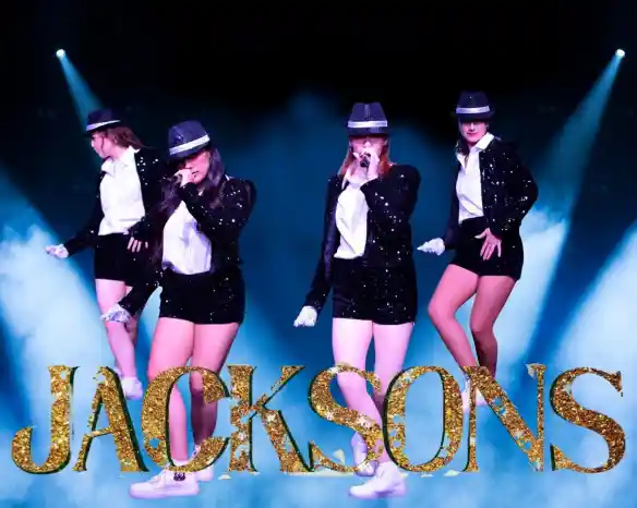 Four performers in sparkling black outfits and hats sing on stage. They are surrounded by blue lights and glitter, with the word "JACKSONS" in gold letters at the bottom.