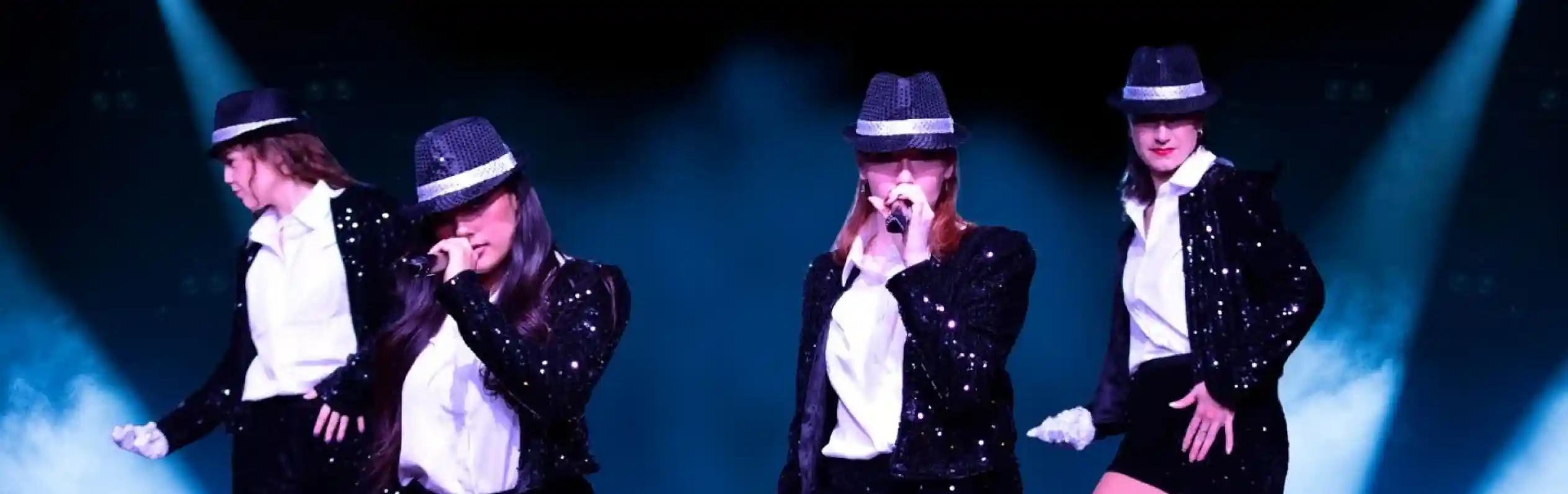 Four performers in sparkling black outfits and hats sing on stage. They are surrounded by blue lights and glitter, with the word "JACKSONS" in gold letters at the bottom.