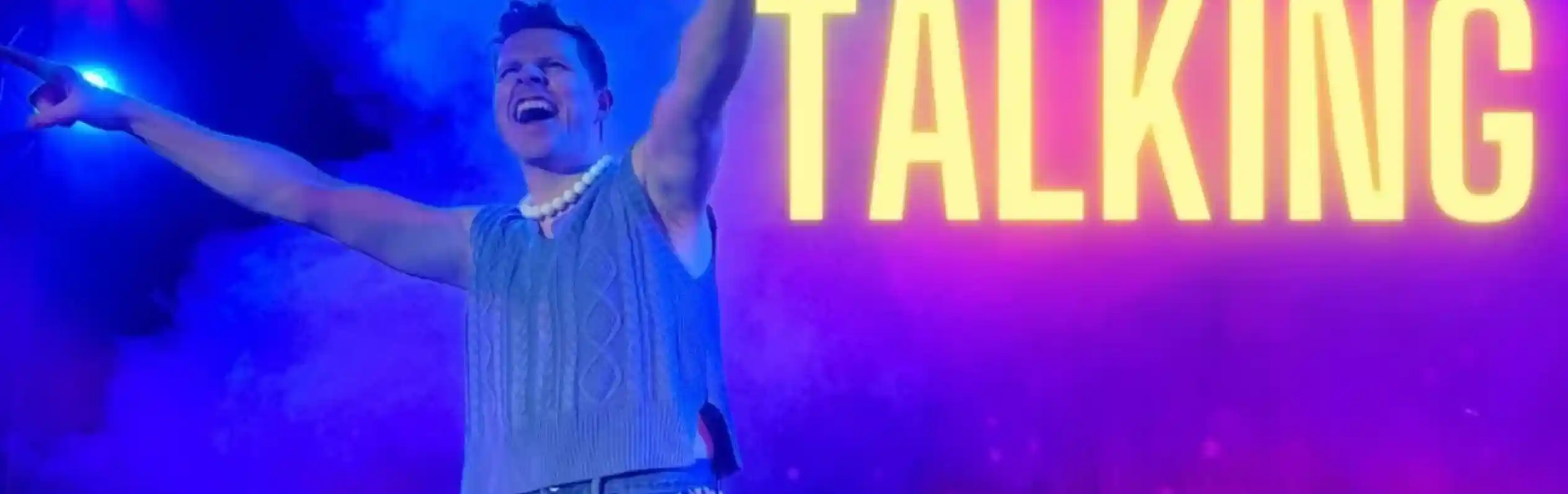 A performer with a joyful expression stands on stage, holding a microphone and wearing a sleeveless sweater and embellished jeans. Colorful lights and smoke create a vibrant atmosphere, with "Late Night Talking" prominently displayed in bold text.