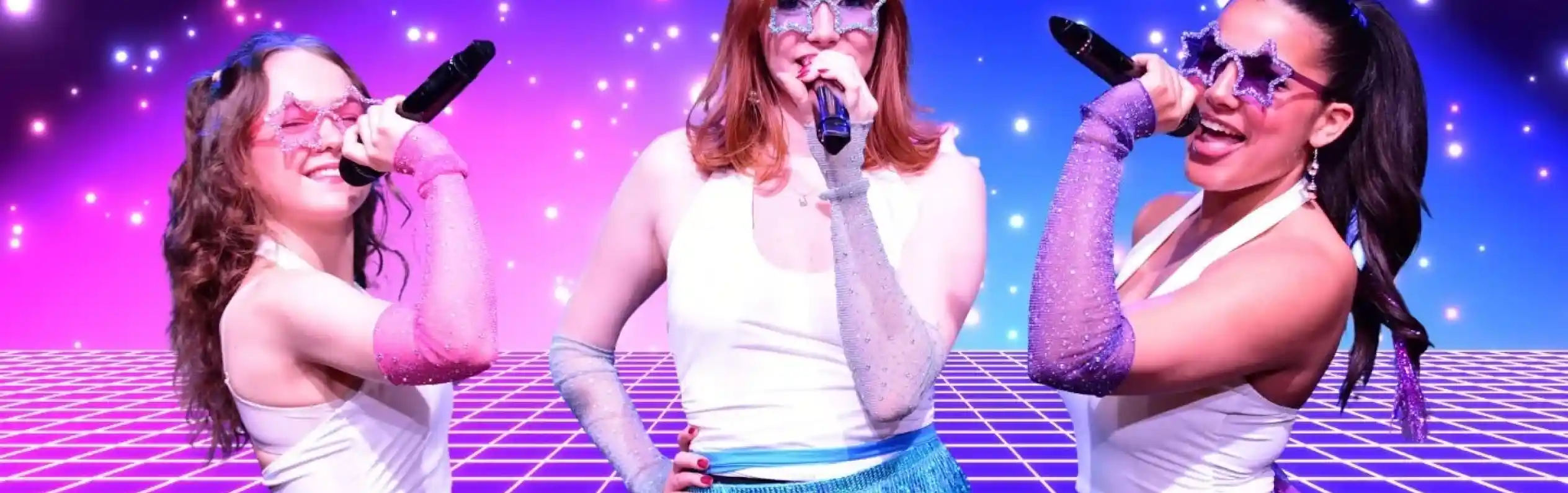 Three performers in shiny, colorful outfits with sparkly skirts and star-shaped sunglasses sing into microphones. They stand against a vibrant, starry background with a grid pattern. The scene has a fun, retro vibe, reminiscent of a disco party.