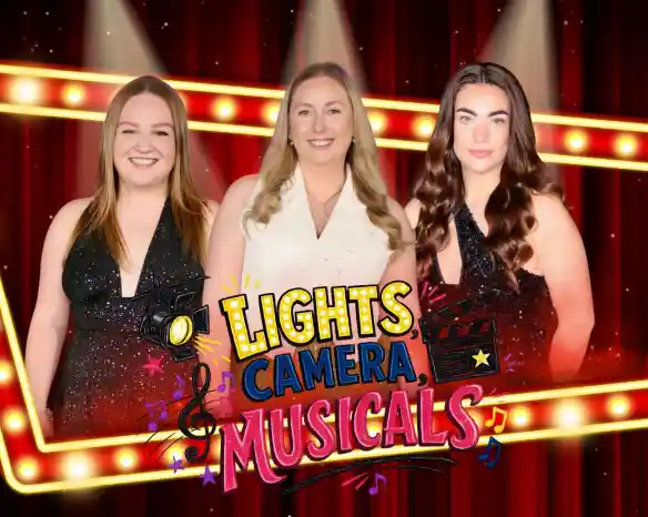 Three smiling women stand against a vibrant backdrop featuring stage lights and musical notes. The text "Lights, Camera, Musicals!" is prominently displayed in colorful letters. The women are wearing sparkly outfits and the setting suggests a theatrical theme.