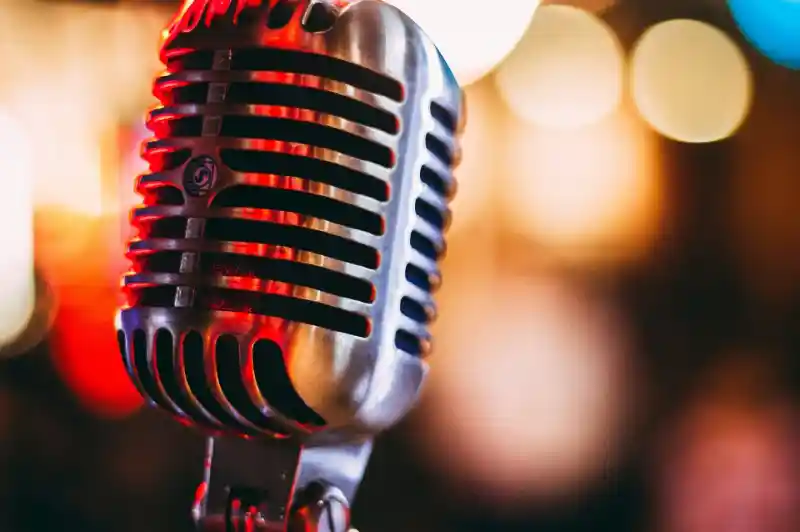 A vintage-style microphone with a shiny metal finish, set against a softly blurred colorful background of lights.