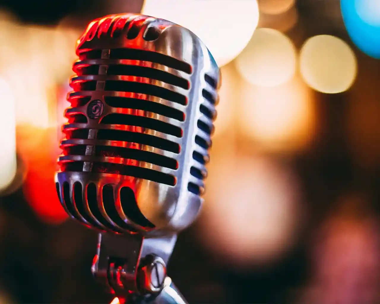 A vintage-style microphone with a shiny metal finish, set against a softly blurred colorful background of lights.