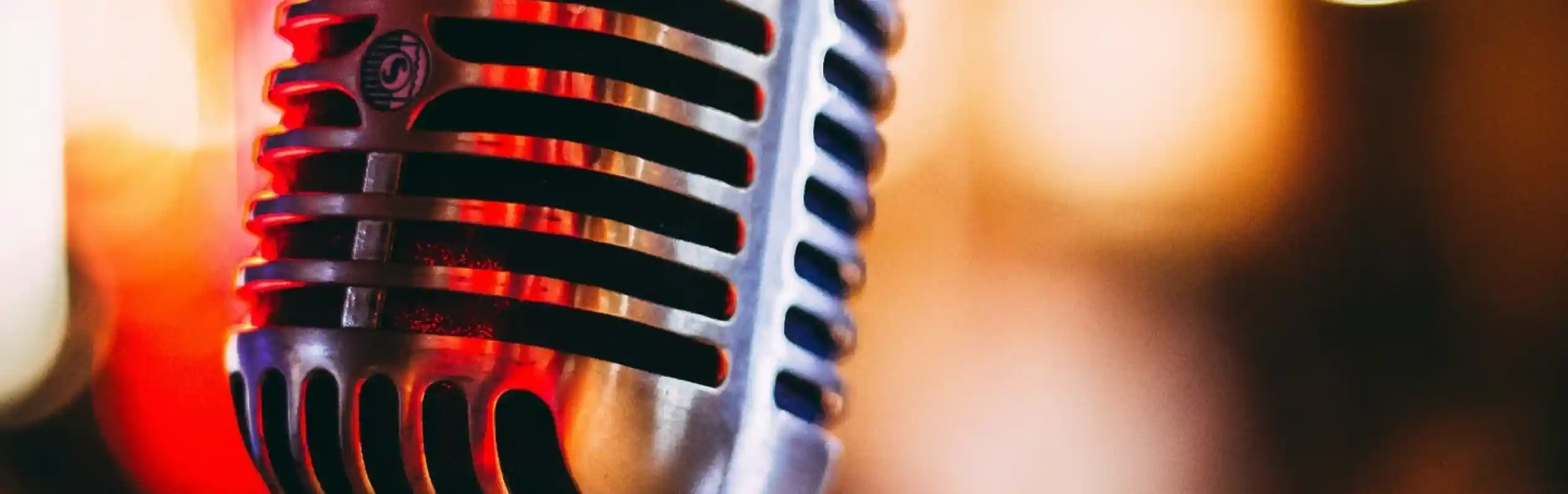 A vintage-style microphone with a shiny metal finish, set against a softly blurred colorful background of lights.