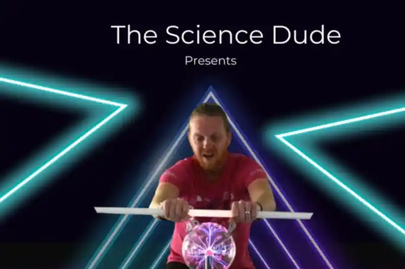 A man in a pink shirt is demonstrating a science experiment involving a clear sphere, surrounded by neon triangular shapes and bright lighting. The text above reads "The Science Dude Presents" and below, "The curious world of."