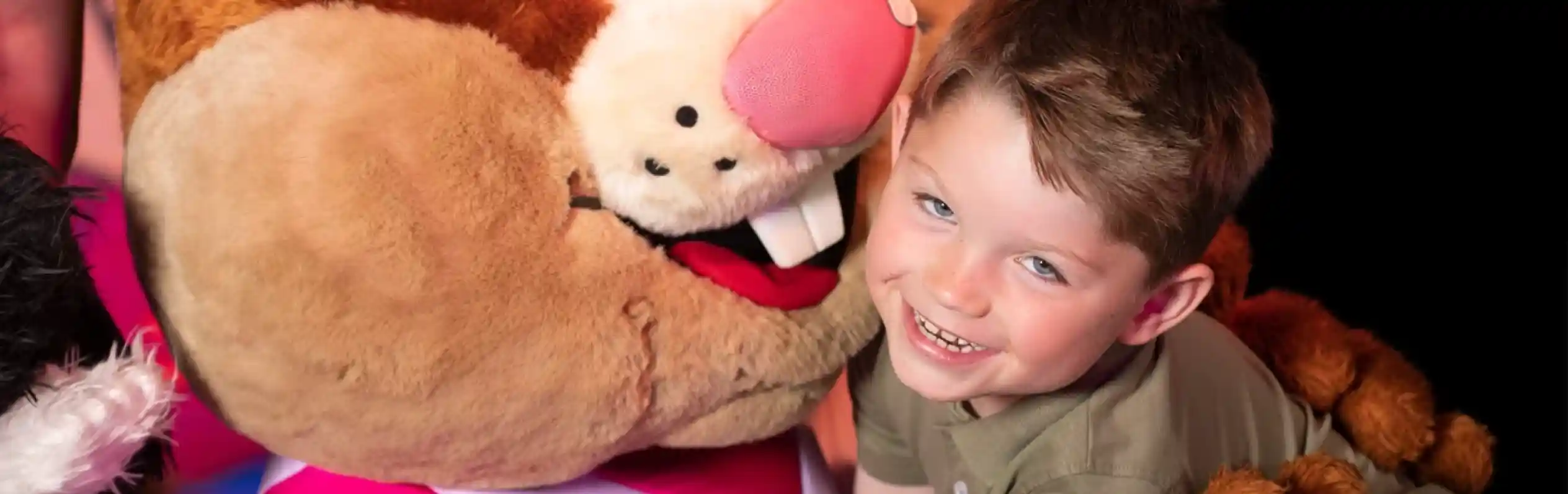 A young boy smiling and hugging a costumed performer in a squirrel outfit.
