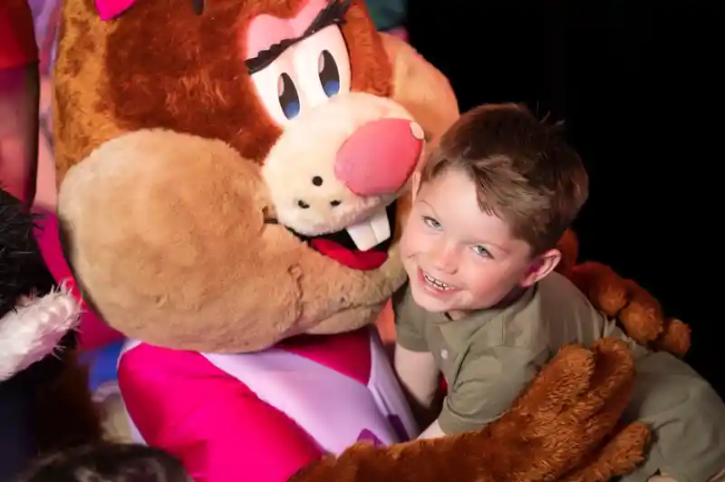 A young boy smiling and hugging a costumed performer in a squirrel outfit.