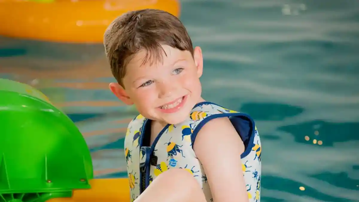 A group of four people, two adults and two children, pose in a colorful room filled with playful decorations. One child holds a large blue sign that reads, "I'm Still Confused," while the others smile and look amused.