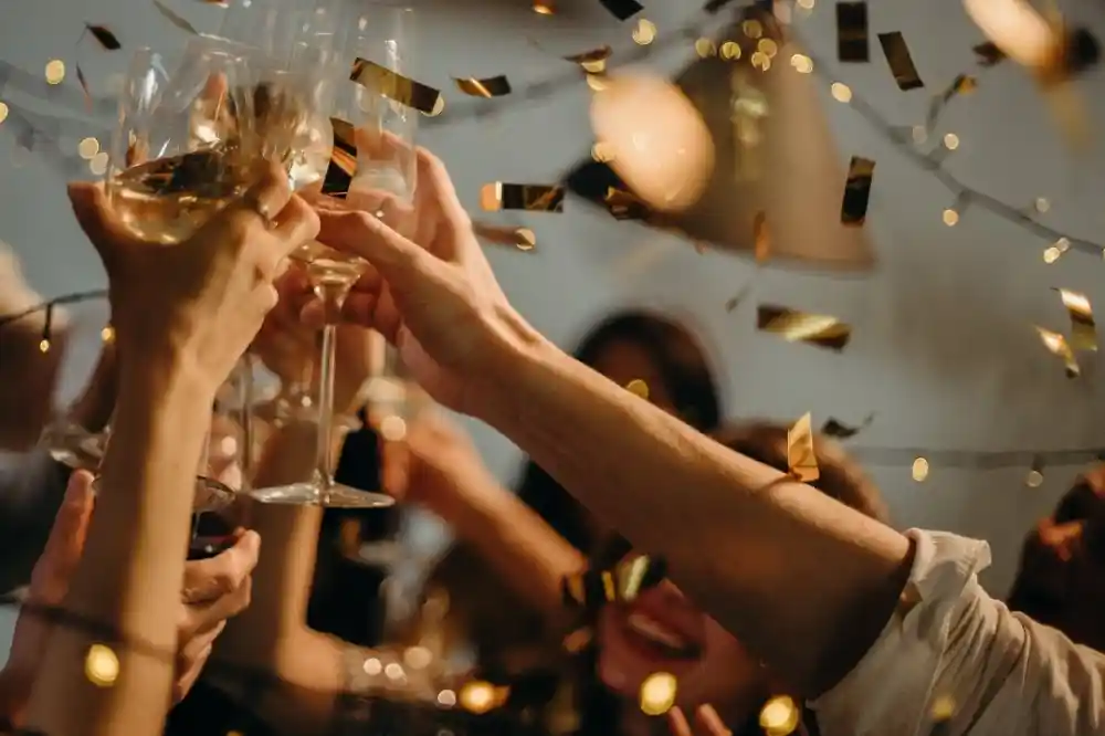 Cheers with glasses filled with champagne, surrounded by confetti and twinkling lights. Friends celebrate joyfully in a festive atmosphere.