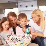 A family of four sits together on a sofa, joyfully decorating colorful Easter eggs in a bright, modern living space. The parents smile at their two children, who are engaged in the activity, showcasing a warm and festive atmosphere.