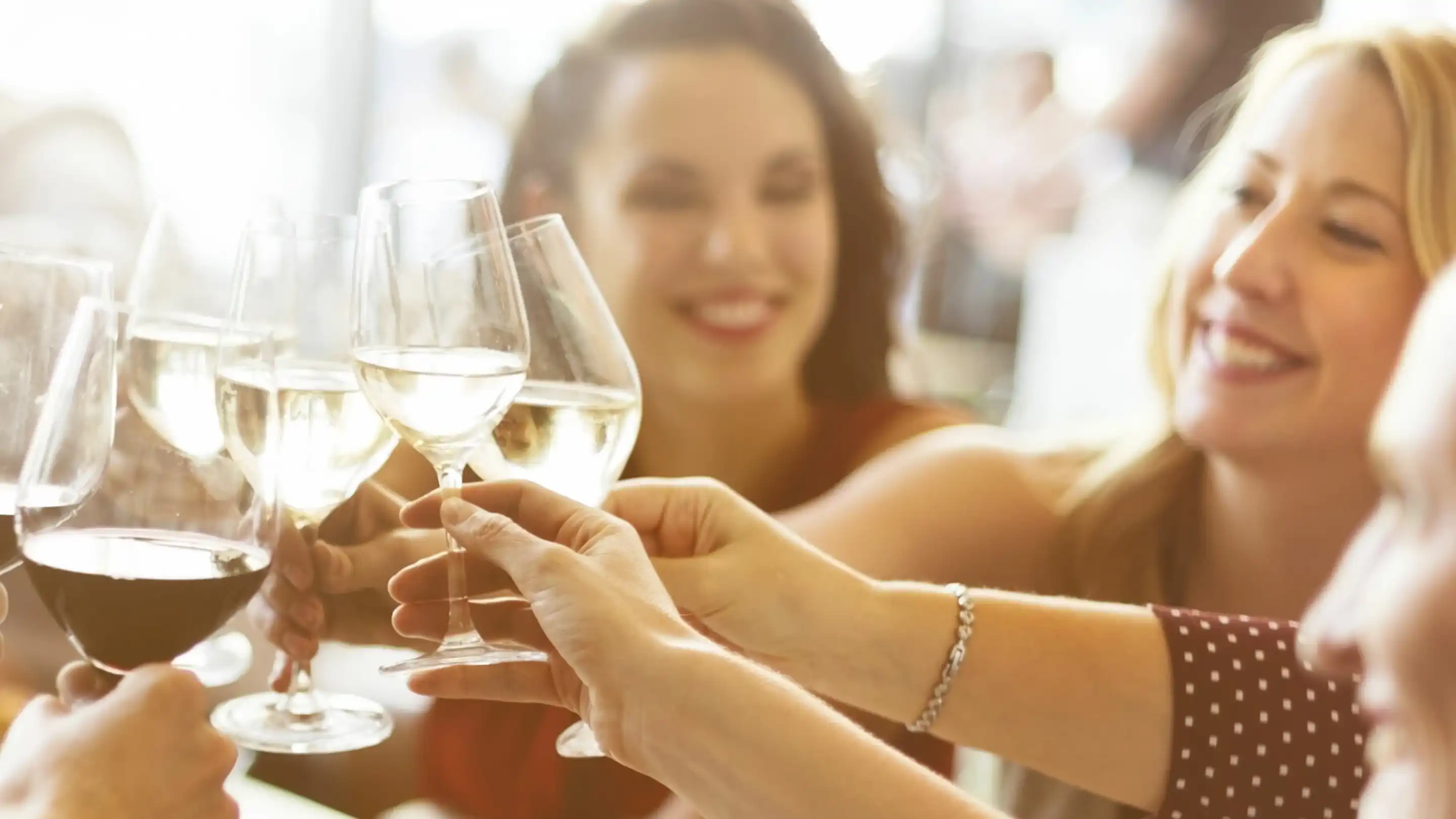 A group of friends toasting with glasses of white wine, smiling and celebrating together in a bright, cheerful atmosphere.