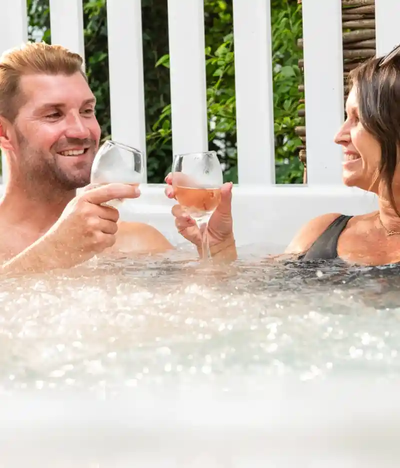 A woman and a man relax on a couch, laughing and enjoying time with a smiling boy who is sitting between them. The boy holds a drink while the woman is looking at him; they are in a bright room with greenery visible outside.