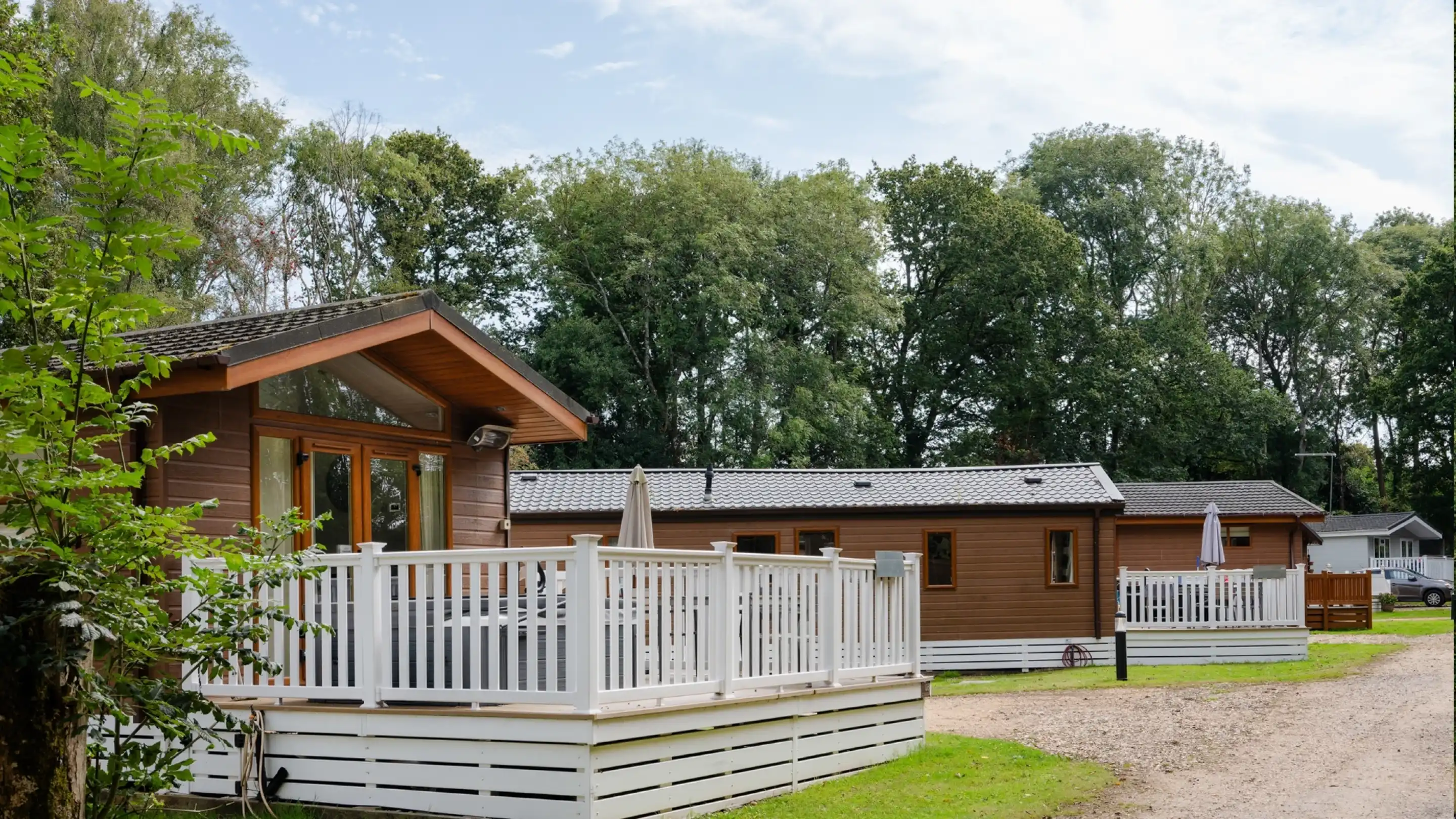 Wooden holiday cabins with porches, surrounded by trees and green grass, lined along a gravel path.