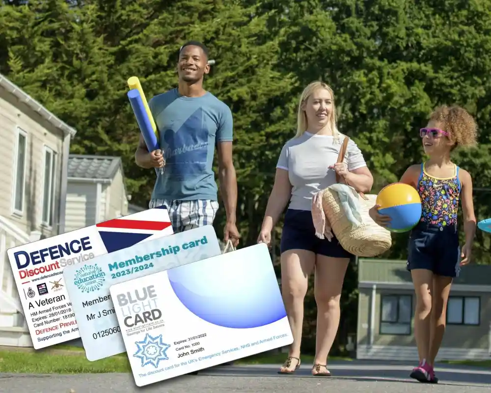 A family walks cheerfully along a path near holiday accommodations, carrying beach balls and a bag. In the foreground, there are two membership cards: one for Defence Discount Service and another for Blue Light Card.