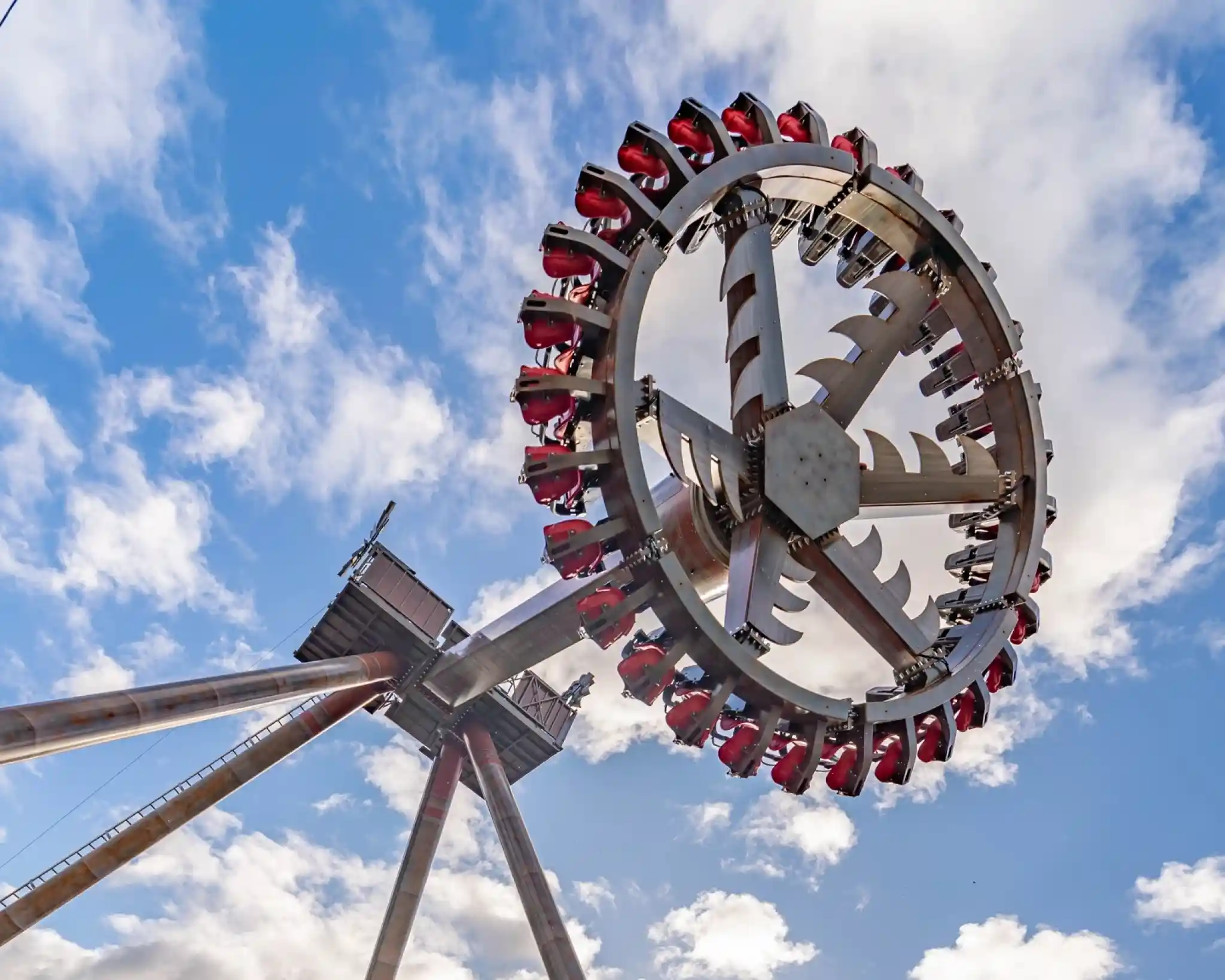 A large amusement park ride featuring a rotating circular structure with seats attached, set against a blue sky with fluffy white clouds.