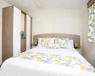 A bright bedroom with a bed dressed in yellow and white bedding, complemented by a wooden dresser nearby.