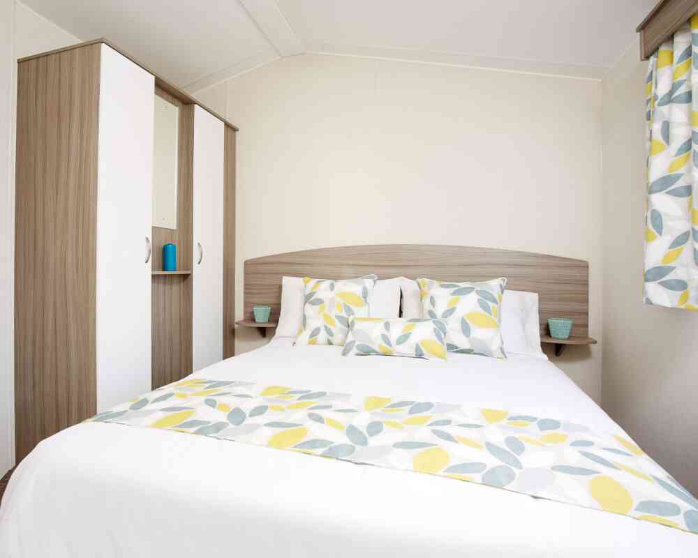 A bright bedroom with a bed dressed in yellow and white bedding, complemented by a wooden dresser nearby.