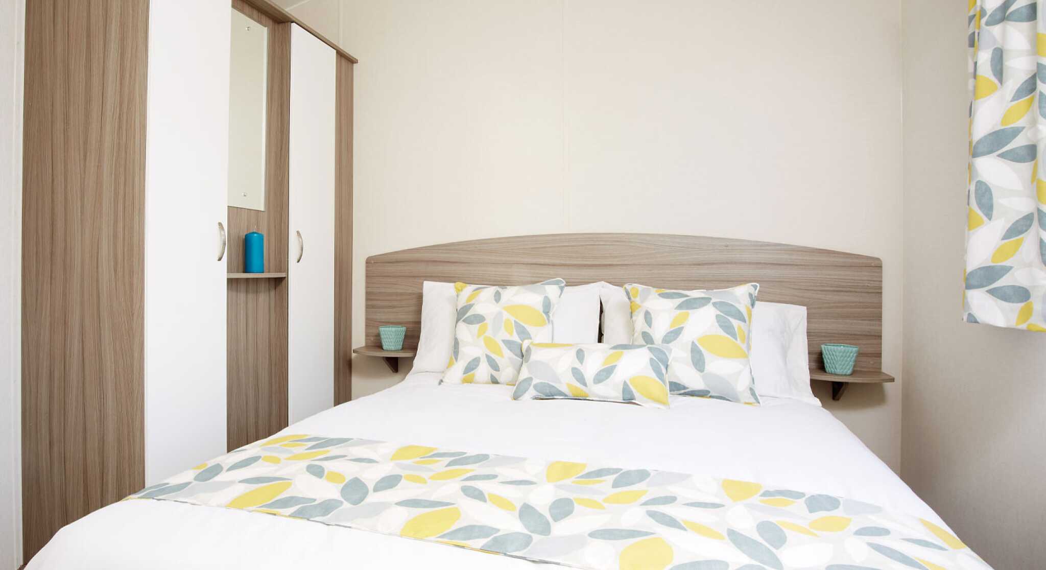 A bright bedroom with a bed dressed in yellow and white bedding, complemented by a wooden dresser nearby.
