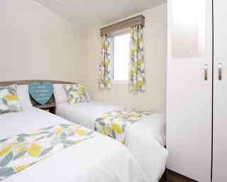 A cosy second bedroom featuring two beds, white walls, and yellow-green curtains.