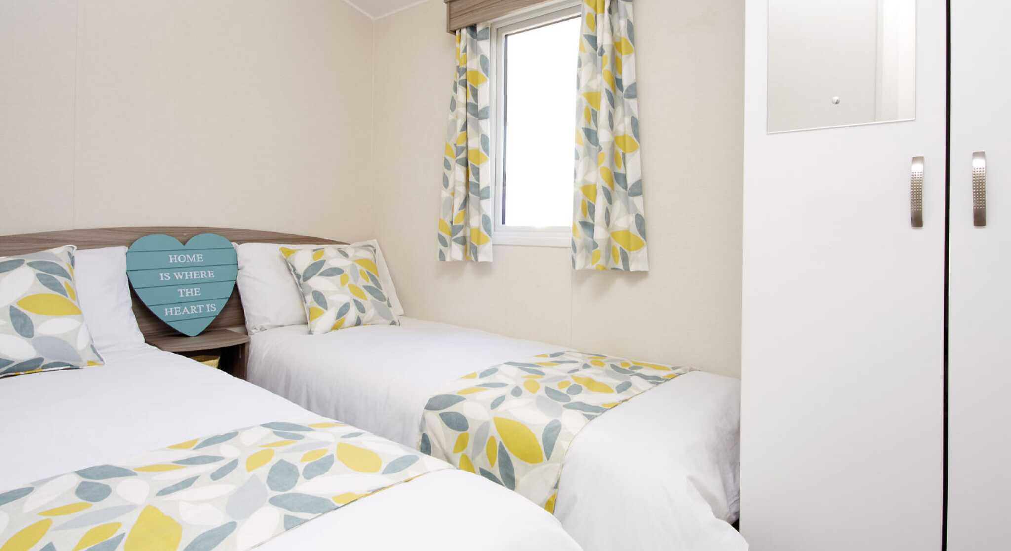 A cosy second bedroom featuring two beds, white walls, and yellow-green curtains.