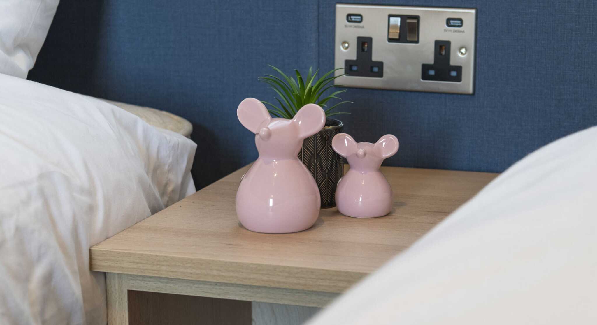 Twin beds with a nightstand between it, featuring a pink mouse ornaments, plant and electric sockets