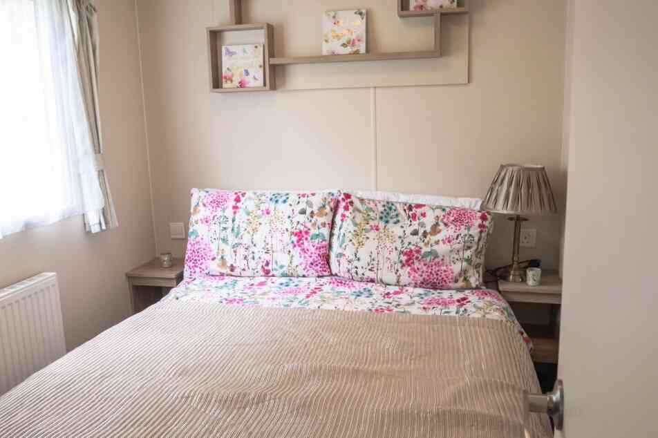 A cosy bed with a floral bedspread positioned near a window, allowing natural light to brighten the room.