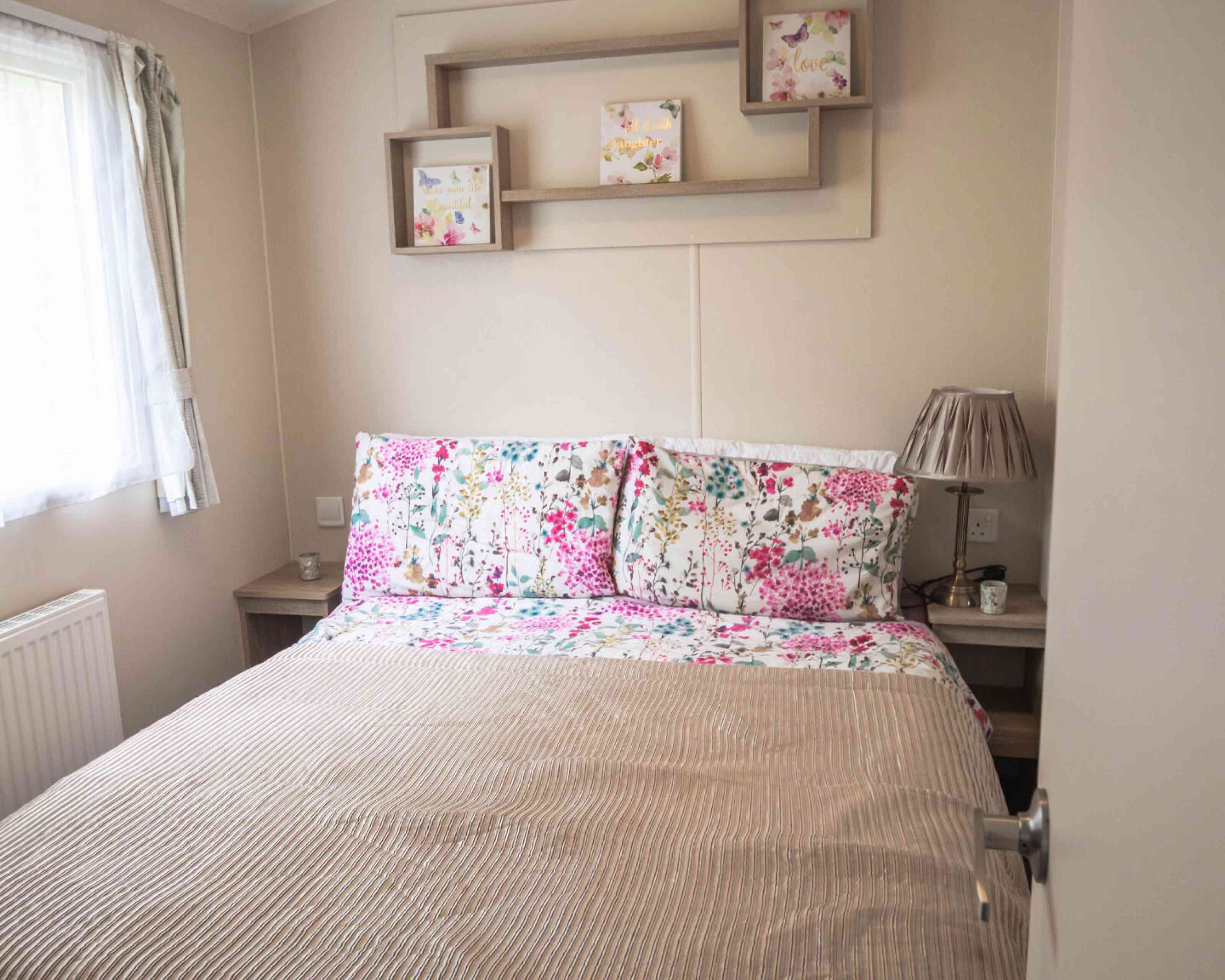 A cosy bed with a floral bedspread positioned near a window, allowing natural light to brighten the room.