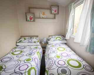 A second bedroom featuring two twin beds, neatly made with simple bedding and a window allowing natural light