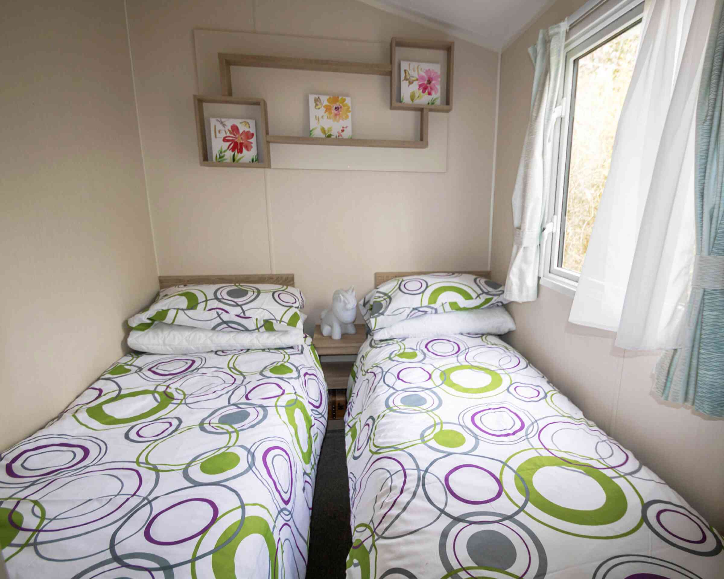 A second bedroom featuring two twin beds, neatly made with simple bedding and a window allowing natural light