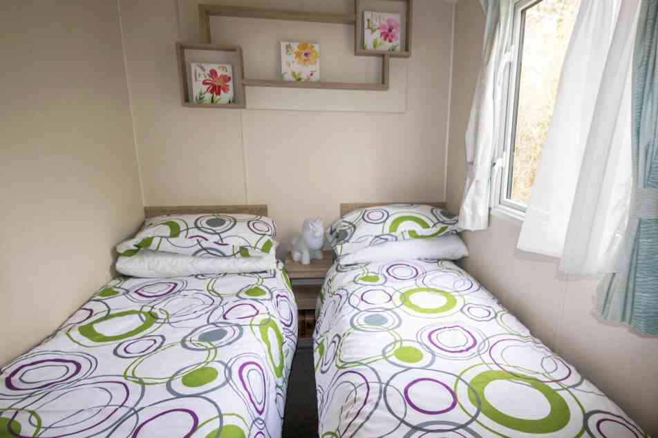 A second bedroom featuring two twin beds, neatly made with simple bedding and a window allowing natural light