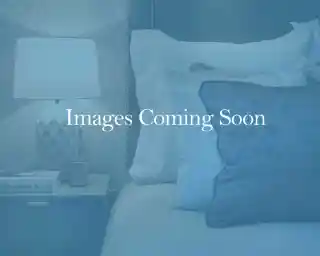 A cozy bedroom scene featuring a neatly made bed with plush pillows and a bedside table topped with a decorative lamp and a small candle. The background suggests a calming ambiance.