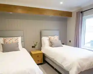 Two twin beds with grey headboards and patterned pillows in a room with wood accents and a large window.