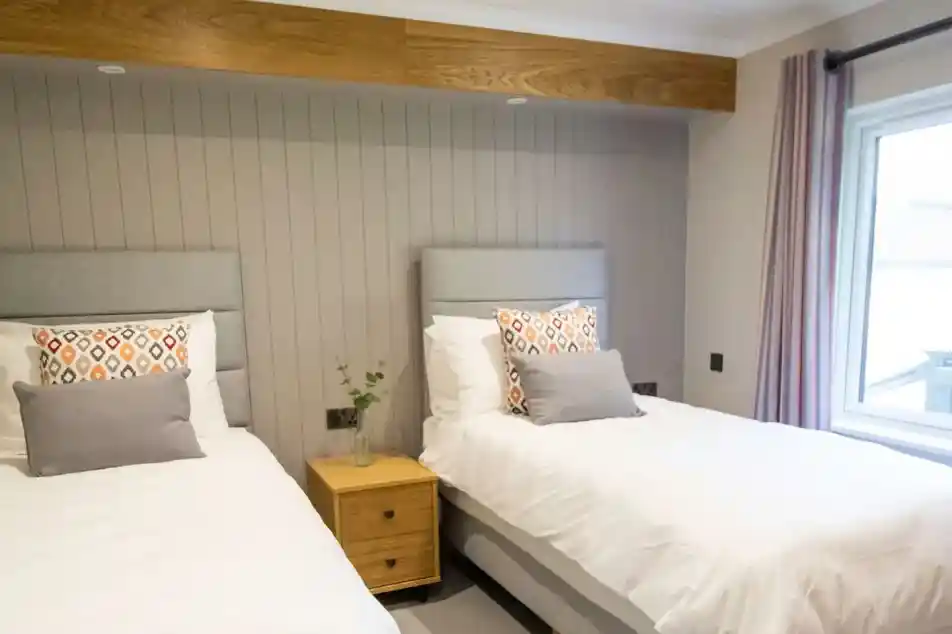 Two twin beds with grey headboards and patterned pillows in a room with wood accents and a large window.