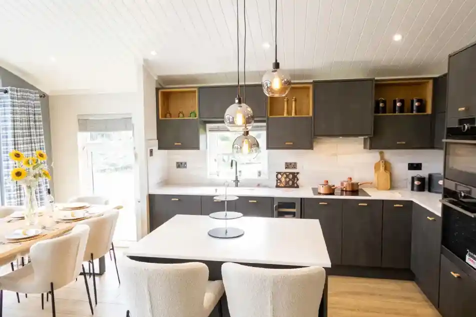 Modern dark grey kitchen with a white island, pendant lights, and a dining area with sunflowers.