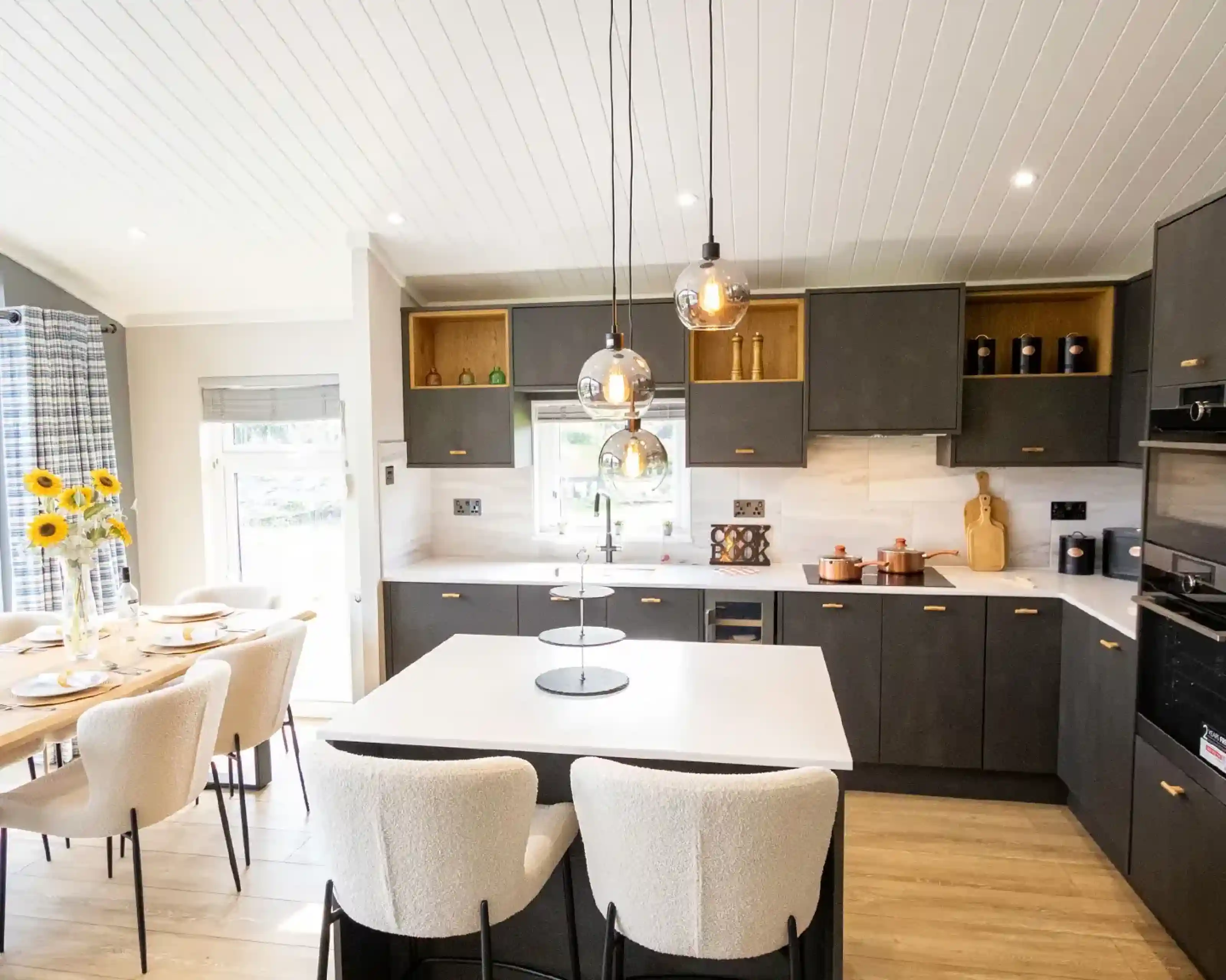 Modern dark grey kitchen with a white island, pendant lights, and a dining area with sunflowers.