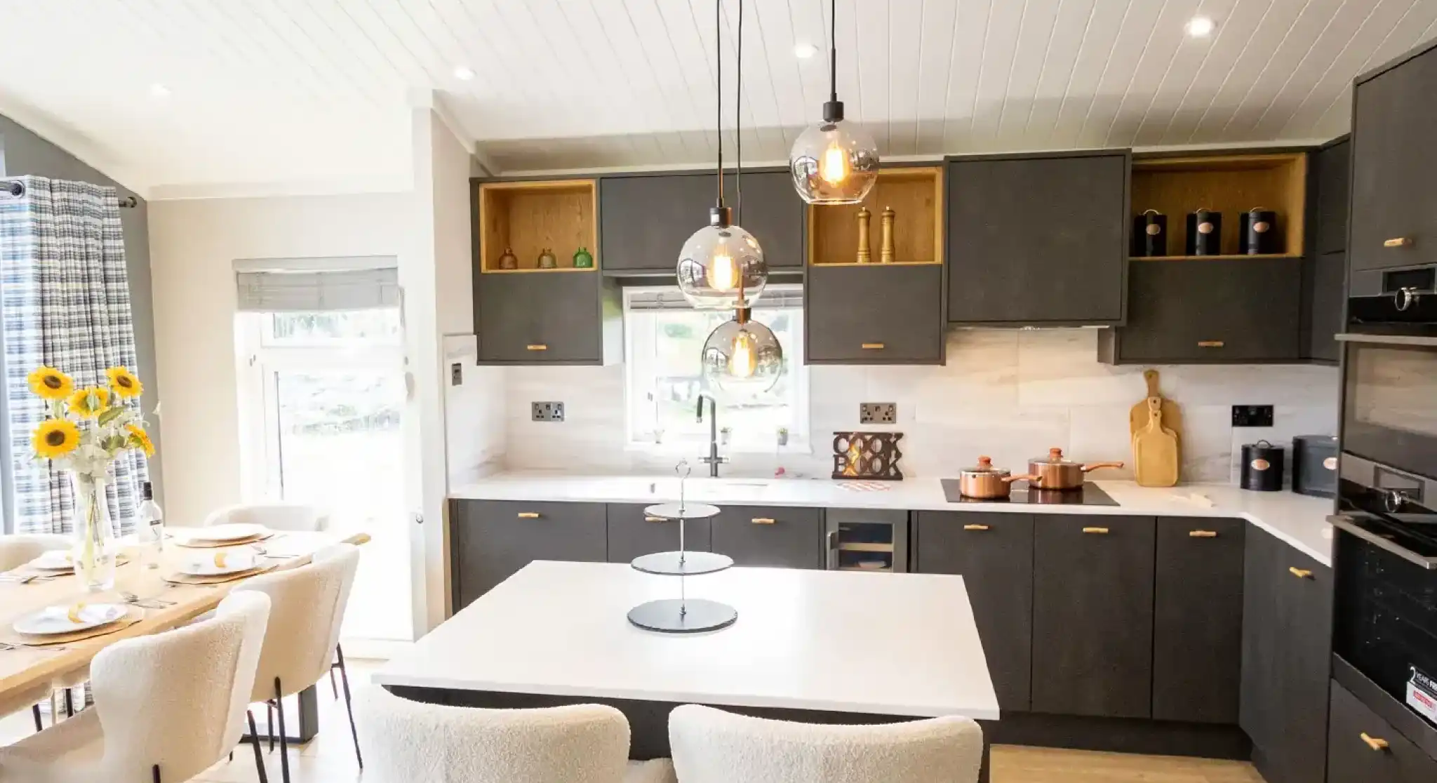 Modern dark grey kitchen with a white island, pendant lights, and a dining area with sunflowers.