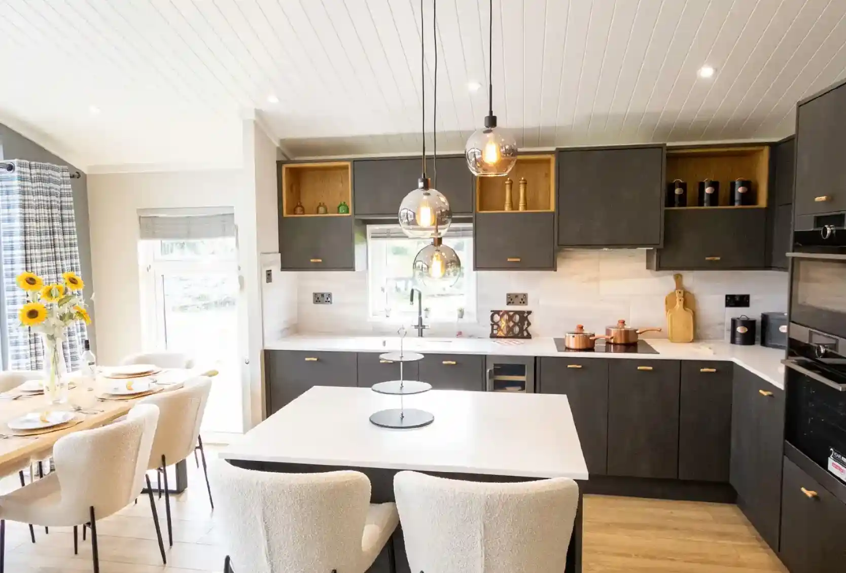 Modern dark grey kitchen with a white island, pendant lights, and a dining area with sunflowers.