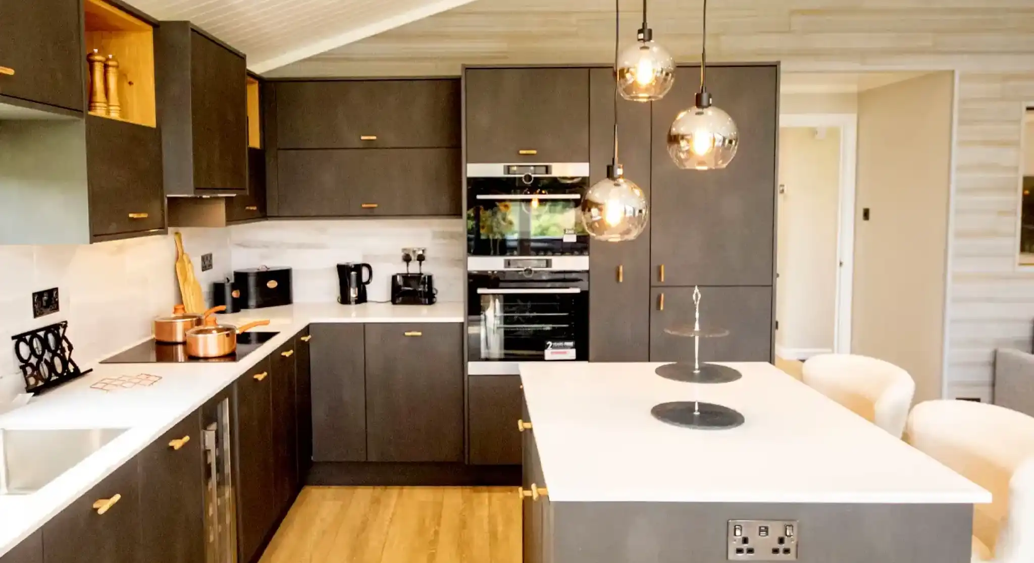 Modern grey kitchen with dark cabinetry, a white island, and pendant lighting.