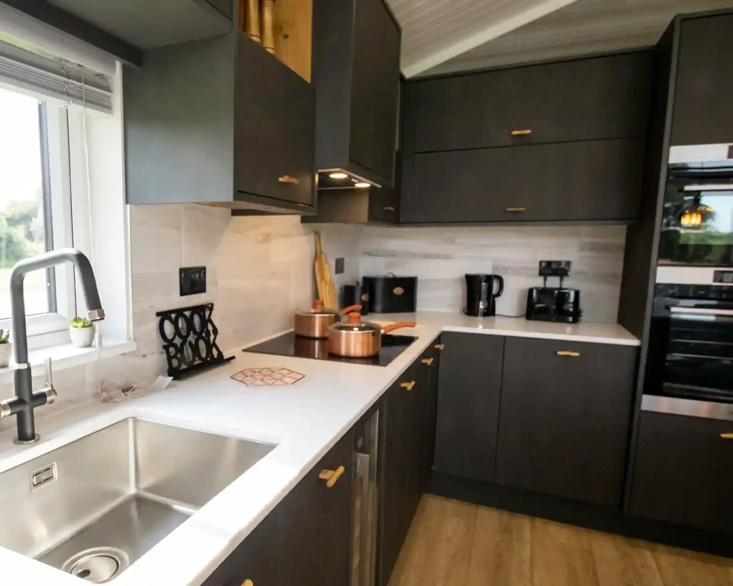 Modern dark grey kitchen with white countertops, copper pots, and a stainless steel sink.