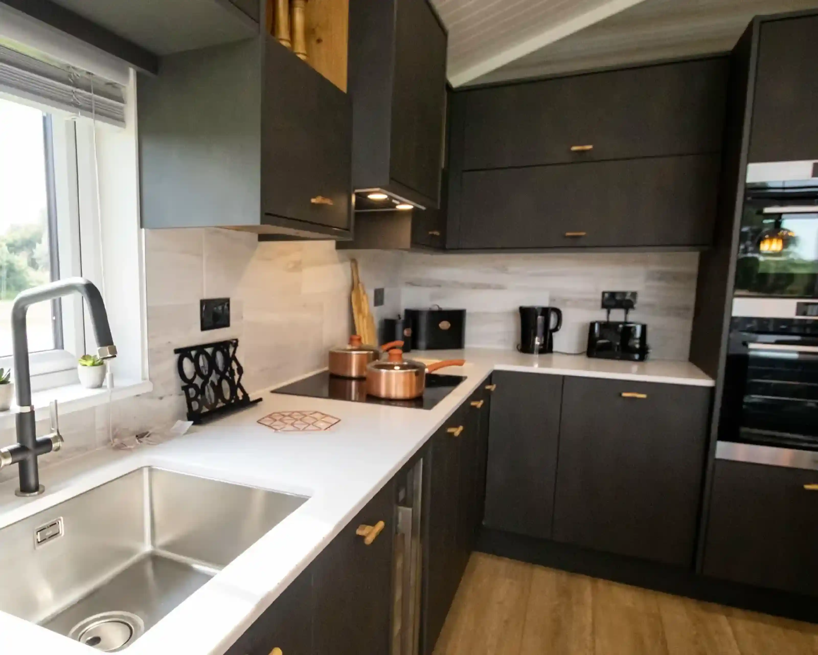 Modern dark grey kitchen with white countertops, copper pots, and a stainless steel sink.