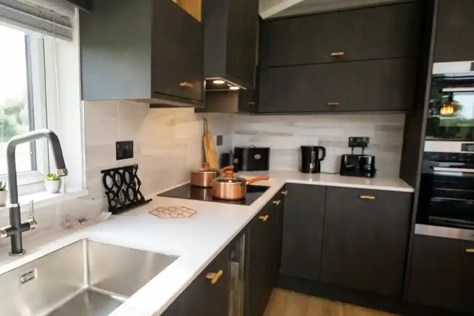 Modern dark grey kitchen with white countertops, copper pots, and a stainless steel sink.