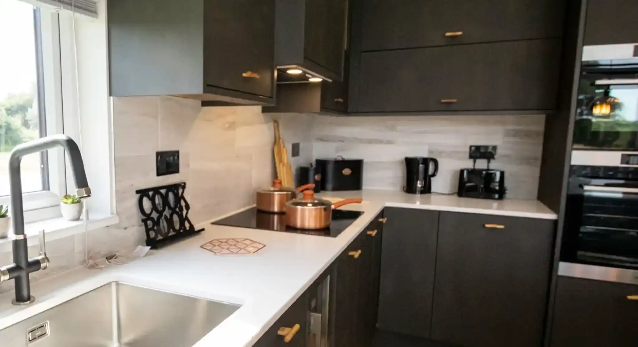 Modern dark grey kitchen with white countertops, copper pots, and a stainless steel sink.