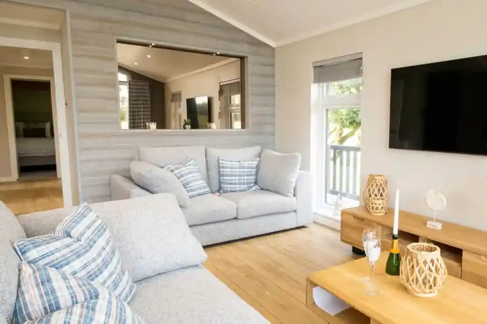 A bright, modern living room with a grey sectional sofa, a large television, and a wooden coffee table with champagne flutes.