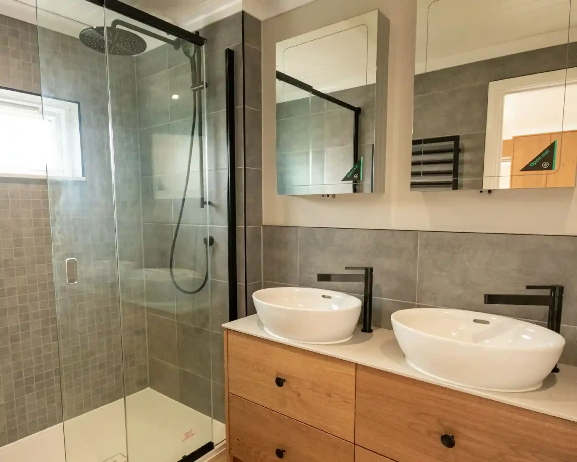 Modern bathroom with a glass-enclosed shower, two white vessel sinks, and wooden vanity cabinets.